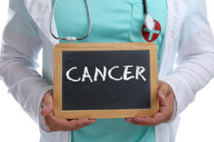A medical doctor wearing a medical coat and stethoscope is holding a board with the text CANCER written on it.