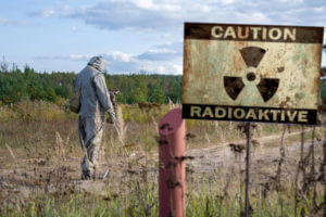 Military dosimetrist measures the radiation area, a sign with the inscription caution, radiation, chemical protectAive suit and gas mask.